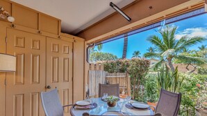 Uma área de refeições com uma mesa posta para quatro pessoas, rodeada por cadeiras, com vista para a vegetação tropical e uma cerca de madeira.