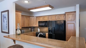 A kitchen with wooden cabinets, a granite countertop, a black refrigerator, a microwave, and a stove. - Riverbend Snowflake Run Condo: At Snowflake Lift (Breckenridge)