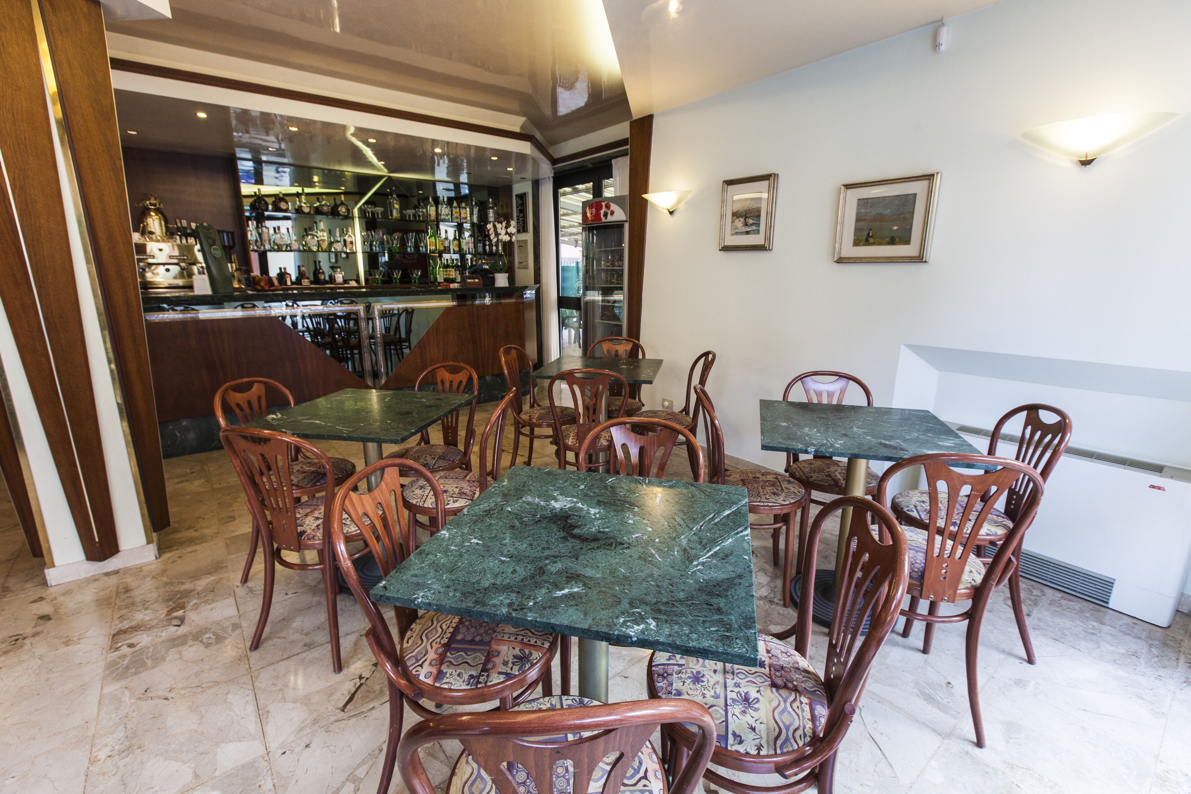 Un espace bar comprenant plusieurs tables et chaises, un comptoir avec diverses bouteilles et un réfrigérateur.