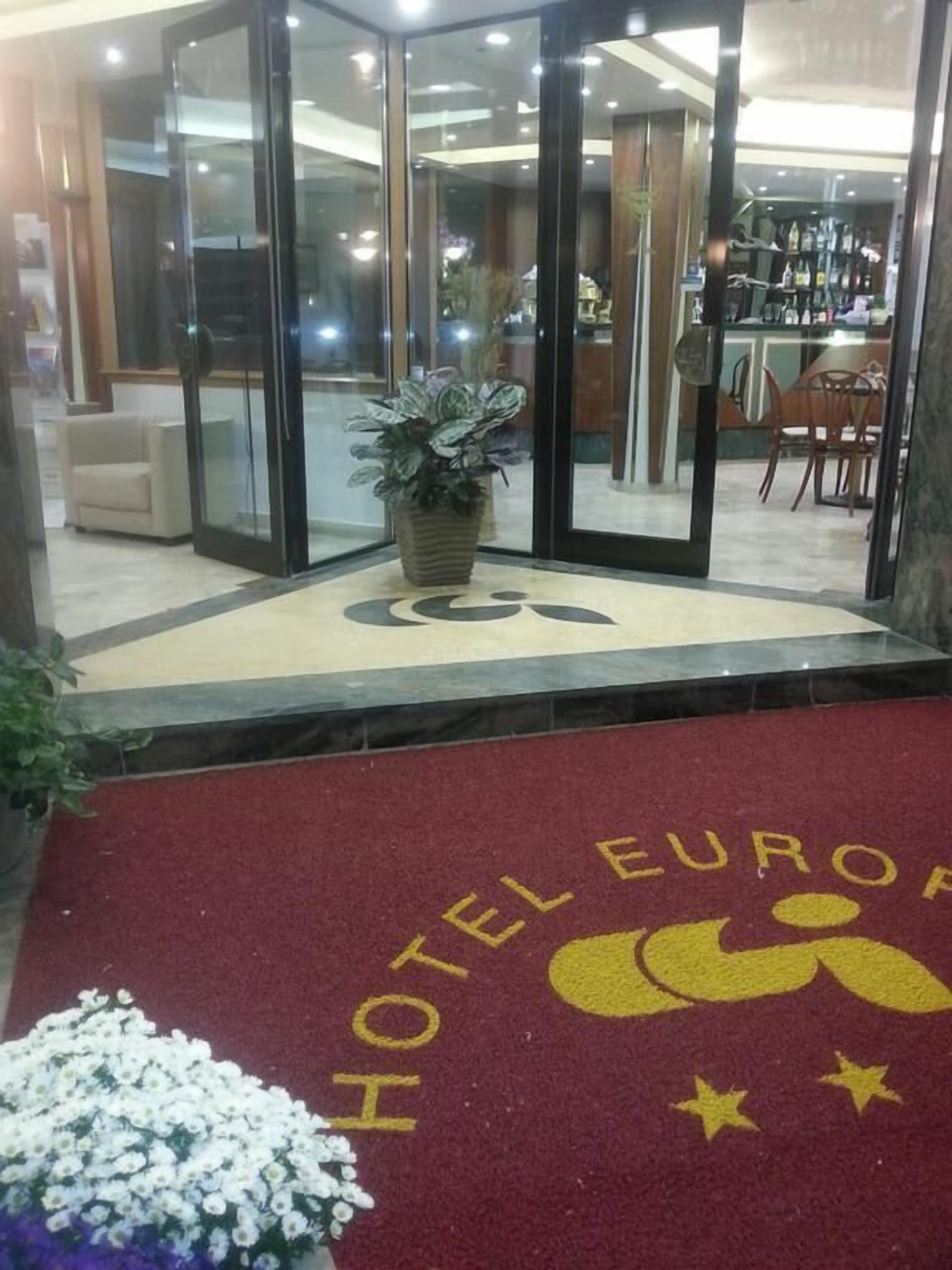 En hotellentrén med en röd matta, en krukväxt och en glasdörr som leder in.