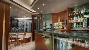 A bar area with a marble countertop, wooden bar stools, and shelves stocked with bottles and glasses. - Hotel Europeo (Chioggia)