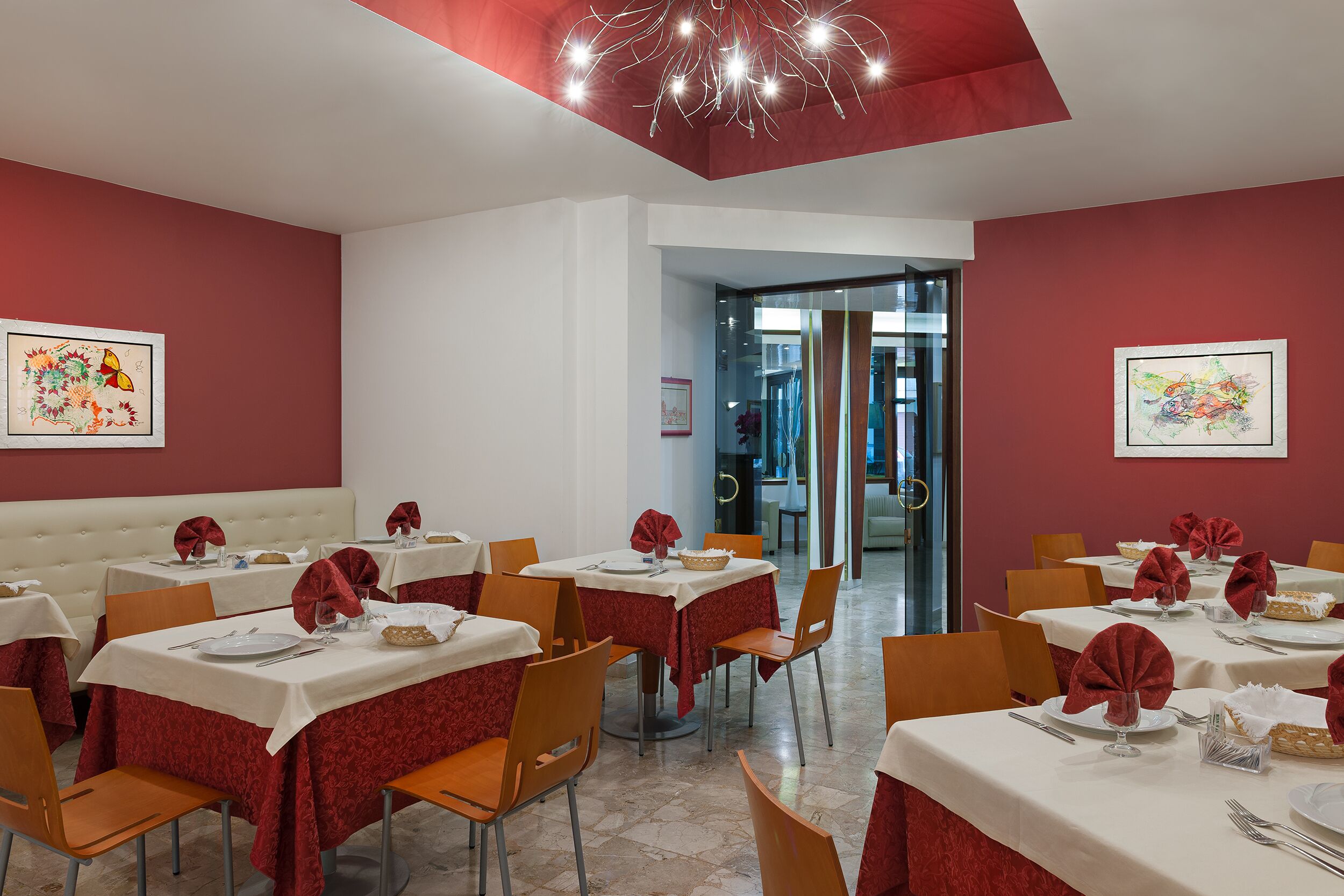 Un restaurant dont les tables sont dressées pour le service, avec des nappes rouges et des chaises orange.