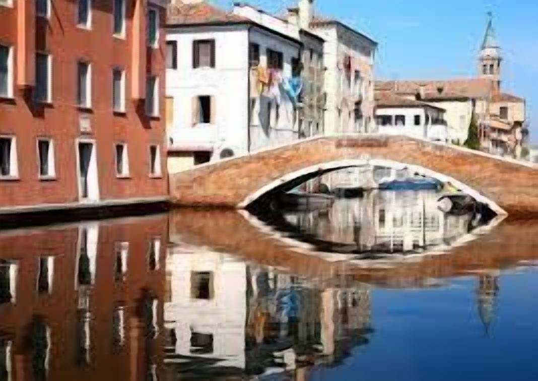 Un canale con un ponte in pietra che riflette edifici e una torre.