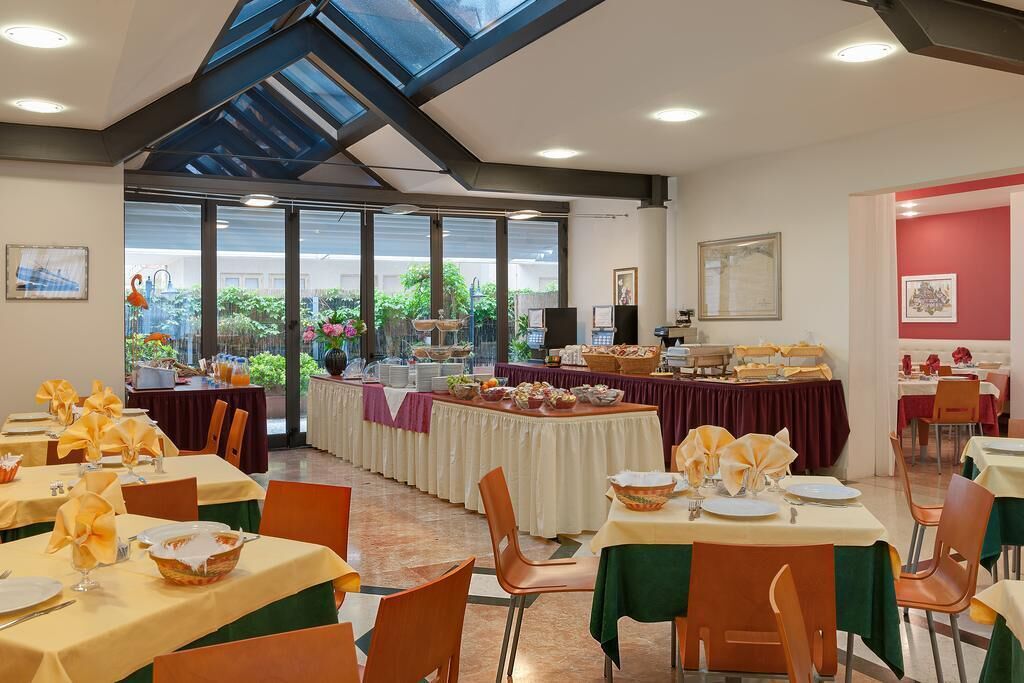 Un espace repas avec des tables préparées pour le petit-déjeuner, un buffet proposant divers plats et une vue sur la verdure environnante.