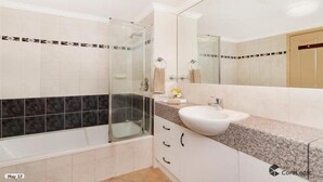 Un bany modern amb una dutxa amb envàs de vidre, un lavabo blanc i un mirall gran.