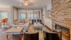 A spacious living room with a fireplace, a stone accent wall, and a large window. - Family Friendly Spacious Home with Backyard Pool by Redawning (Frisco)