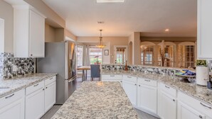 A modern kitchen with white cabinetry, granite countertops, and a central island. - Family Friendly Spacious Home with Backyard Pool by Redawning (Frisco)