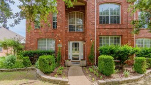 A red brick building with a central entrance, a small porch, and a pathway leading to the door. - Family Friendly Spacious Home with Backyard Pool by Redawning (Frisco)