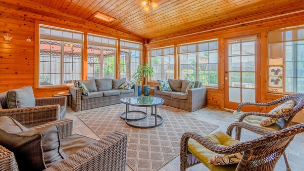 A spacious wooden interior with wicker furniture, large windows, and a central glass coffee table. - Family Friendly Spacious Home with Backyard Pool by Redawning (Frisco)
