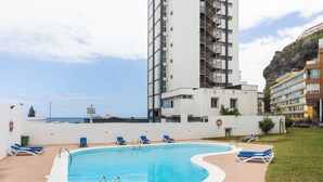 Una piscina sul tetto con poltrone da relax blu, un edificio bianco con facciata bianca e vista sul mare.