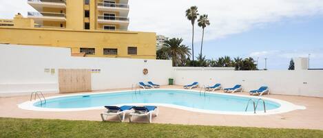 A swimming pool with lounge chairs, a grassy area, and a tall building in the background.