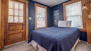 A bedroom with a bed, a wooden door, and a window with blinds. - The Lakeview Cottage 9 (Laconia)