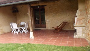 Un patio cubierto con una mesa y sillas, un banco de madera y un muro de piedra.