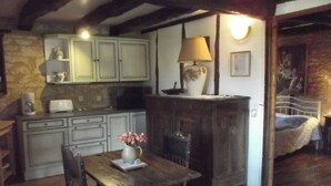 Una cocina rústica con armarios blancos, una mesa de comedor de madera y un jarrón con flores, además de una lámpara sobre un aparador.