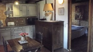 Una cocina rústica con armarios de madera, una mesa con un florero y una cama en la habitación contigua.
