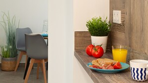 Ein Essbereich mit Tisch, Stühlen, einer Topfpflanze, einer Tomate, einem Glas Orangensaft und einem Teller mit Essen.