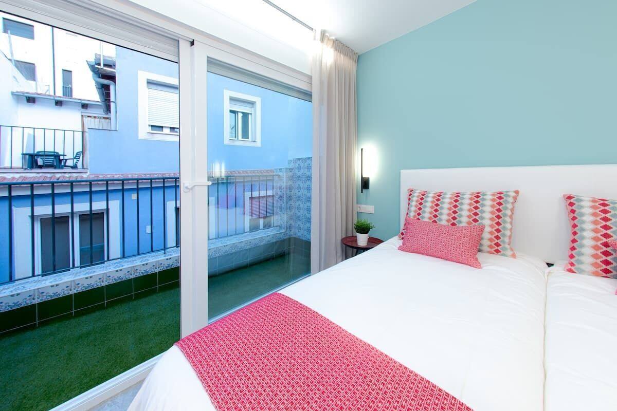 A bedroom with a large bed, a view of a balcony, and a small table with a plant.