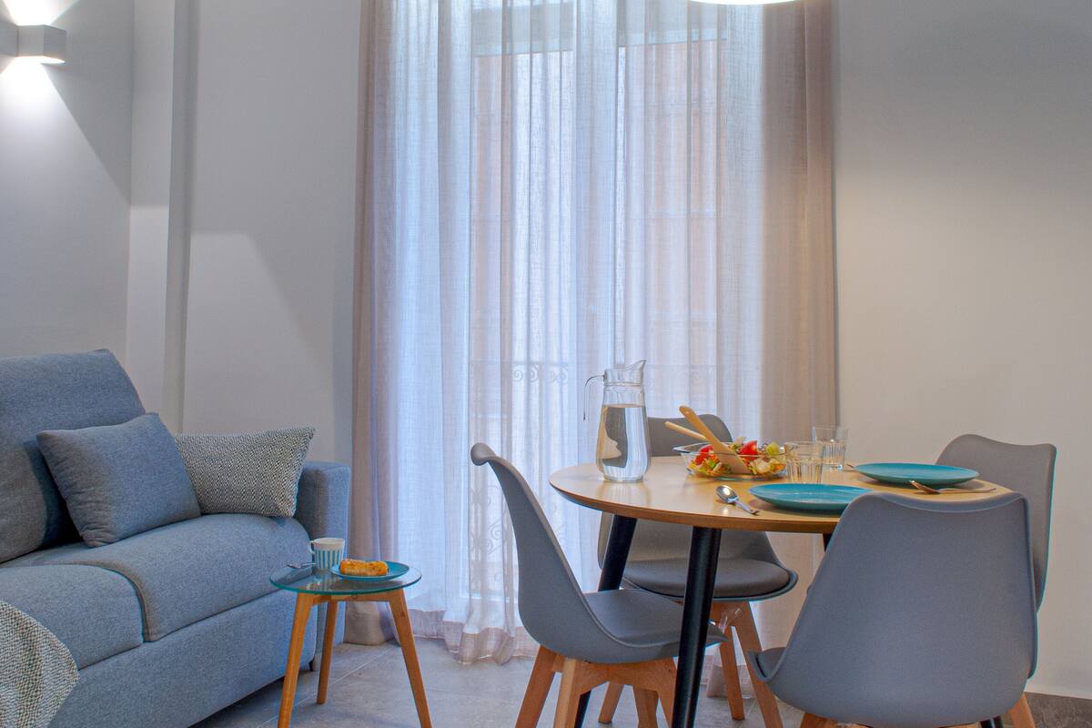 A dining area with a table set for two, a blue sofa, and a modern pendant light.