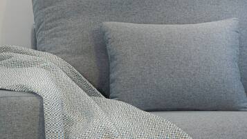 A grey sofa with a patterned throw blanket and a glass coffee table with a blue and white mug.