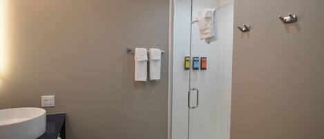 A modern bathroom with a glass shower door, a white sink, and a towel rack with multiple towels.