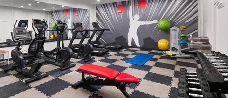 Une salle de sport équipée de tapis de course, de vélos elliptiques, d’un banc de musculation et d’haltères.