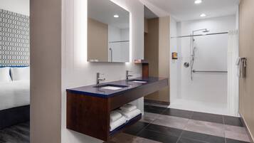 A modern bathroom with a double sink vanity, a large mirror, a shower area, and a tiled floor.
