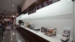 Un espace petit-déjeuner propre et moderne, doté d’un long comptoir, de différents distributeurs de nourriture et d’un mur recouvert de carreaux.