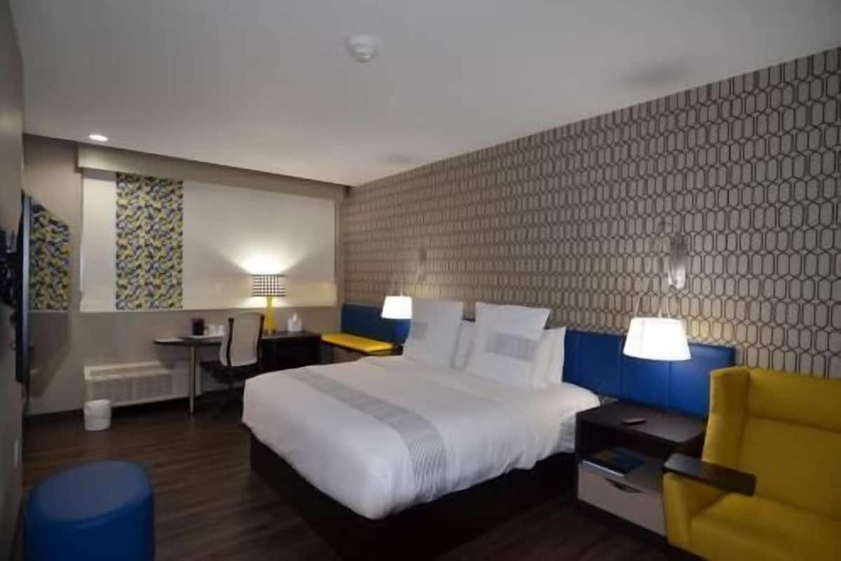 A hotel room with a bed, bedside tables, a desk, a chair, and a patterned wall.