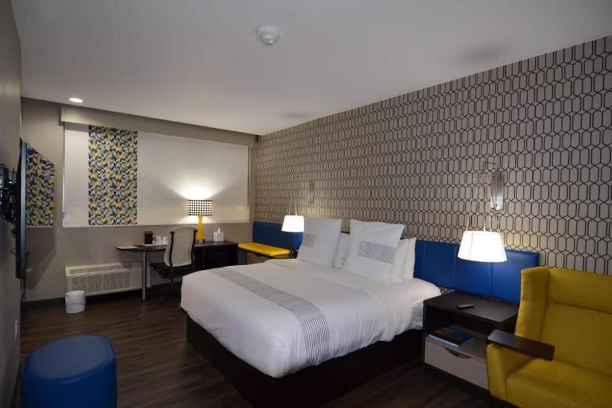 A hotel room with a large bed, two bedside tables, a desk, a chair, and a patterned wall.