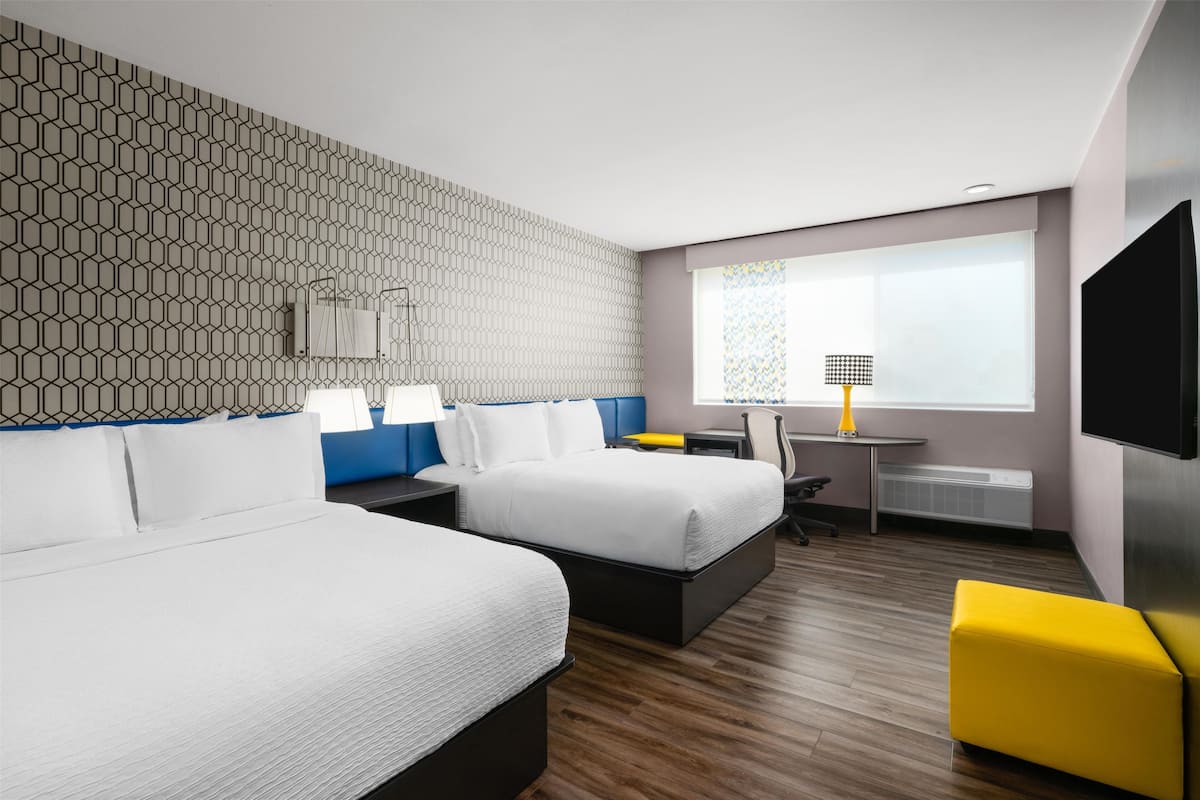 A hotel room with two beds, a desk, a chair, a TV, and a window with a view.