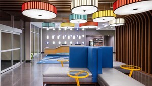 Een moderne lobby met een receptiebalie, een zithoek en kleurrijke hanglampen.