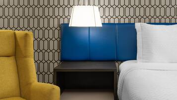 Une chambre d’hôtel avec un mur orné d’un motif géométrique, une tête de lit bleue, un lit blanc et un fauteuil jaune.