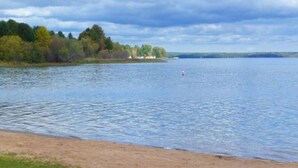 Ein ruhiger See mit sandigem Ufer und einer Baumreihe im Hintergrund.