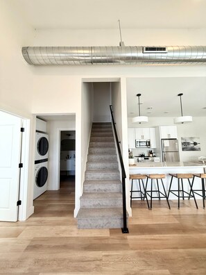 Un intérieur moderne avec un escalier menant à une cuisine, une buanderie et un bar doté de tabourets.