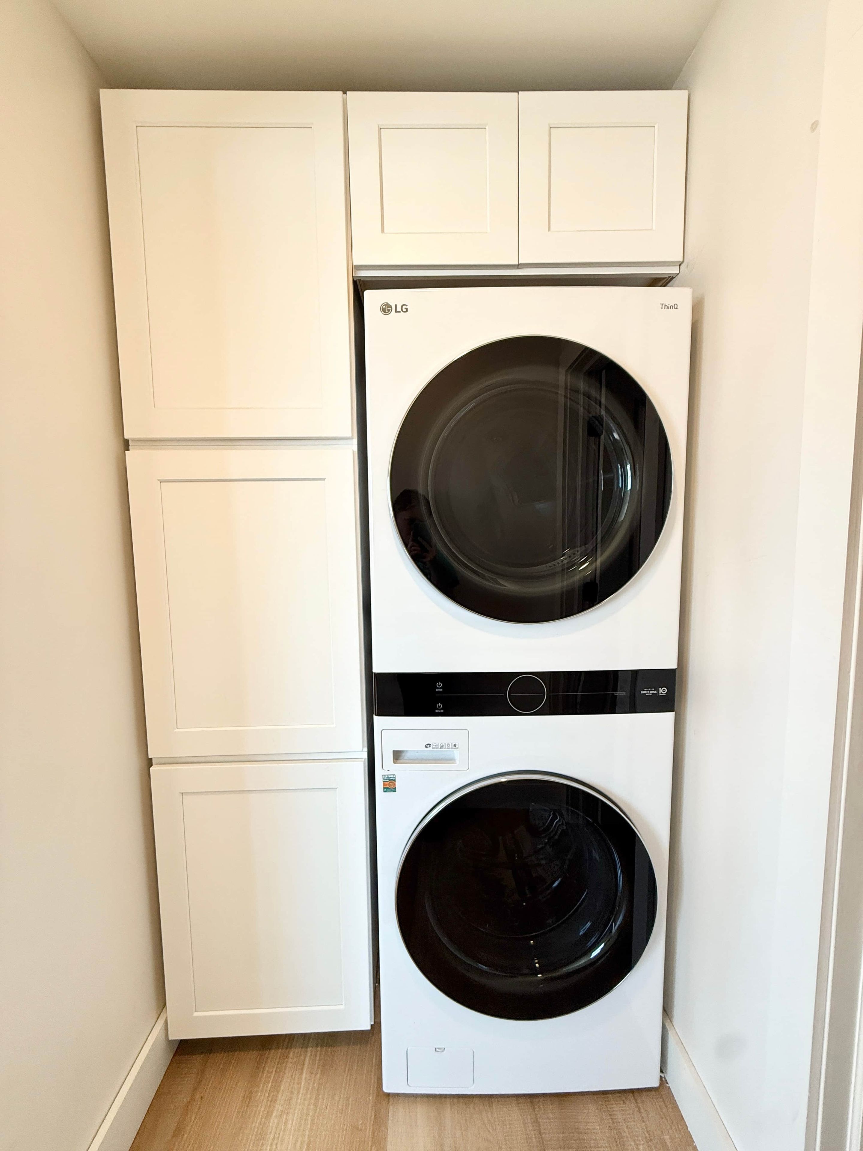 Une petite buanderie équipée d’un lave-linge et d’un sèche-linge à chargement frontal, de meubles blancs et d’un plancher en bois.
