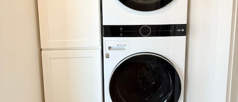 Ein kleiner Hauswirtschaftsraum mit einer Waschmaschine und einem Trockner mit Frontlader, weißen Schränken und Holzboden.