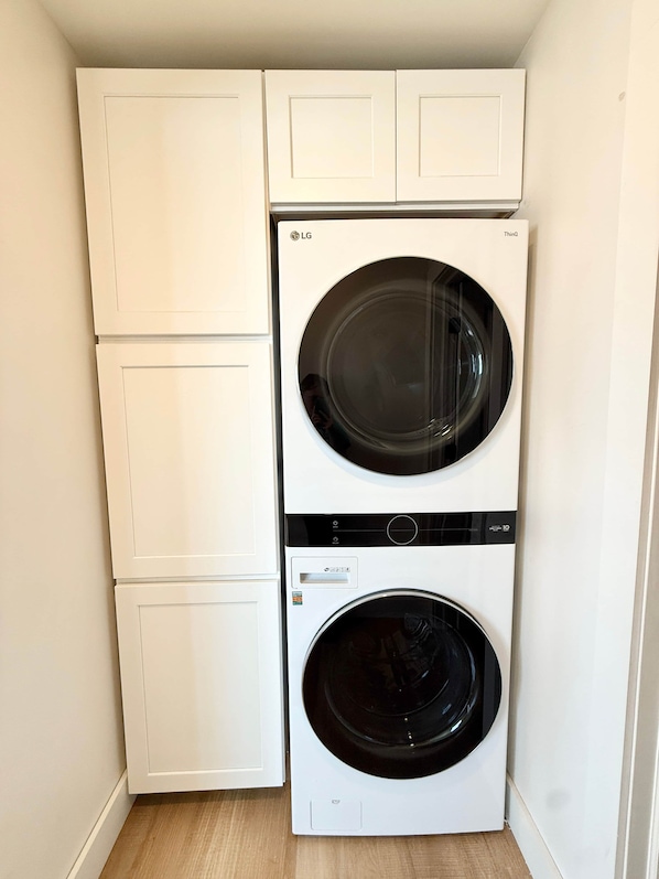 A compact laundry room with a front-loading washer and dryer, white cabinetry, and a wooden floor.