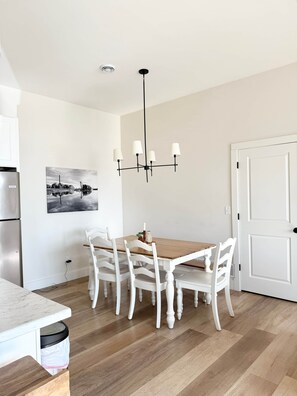 Ein Essbereich mit Holztisch, weißen Stühlen, einer Kristallleuchtre und einem Wandbild.