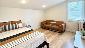 Ein Schlafzimmer mit einem großen Bett, einer Couch, einem kleinen Tisch und einem Fenster mit Jalousien.