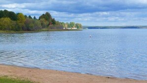 Ein See mit sandigem Ufer und bewaldeter Landschaft im Hintergrund.