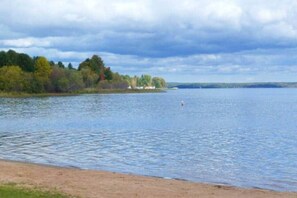 Ein See mit sandigem Ufer und bewaldeter Landschaft im Hintergrund.