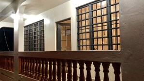Fachada de edifício com três janelas grandes, guarda-corpo de varanda em madeira e parede branca.