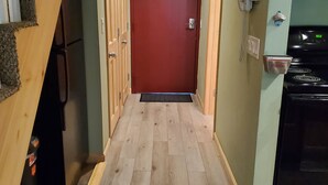 A narrow hallway with wooden flooring, a red door at the end, and a kitchen area with a stove on the right. - Nice Condo At Attitash Mountain Village, Close to Storyland, Location! (Bartlett)