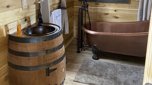 Un baño rústico con un lavamanos en forma de barril de madera, una bañera de cobre y un cuadro con temática de osos en la pared.