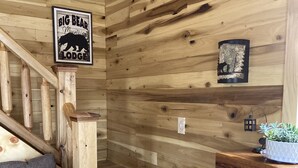 Un interior de madera con una escalera, un sofá, un cartel que dice "Big Bear Mountain Lodge" y una chimenea de piedra.