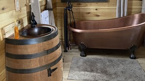 Un baño rústico con un lavamanos de barril de madera, una bañera de cobre y un cuadro de un oso en la pared.