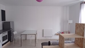 Eine moderne, minimalistische Küche mit weißen Geräten, ein Essbereich mit weißem Tisch und Stühlen sowie ein großes Fenster mit Blick.