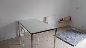 Ein Zimmer mit einem weißen Tisch, einem Heizkörper, einem grauen Teppich und einem Regal mit Büchern und einer kleinen Pflanze.