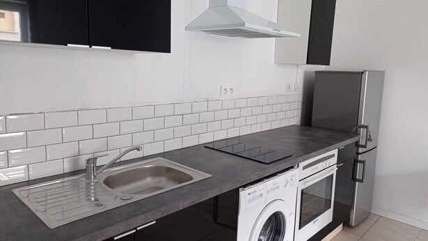 Eine moderne Küche mit Spüle aus Edelstahl, Geschirrspüler, Backofen und Kühlschrank in Schwarz.