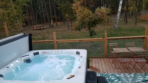Una banyera d'hidromassatge en un terrat de fusta amb vista a una zona boscosa.